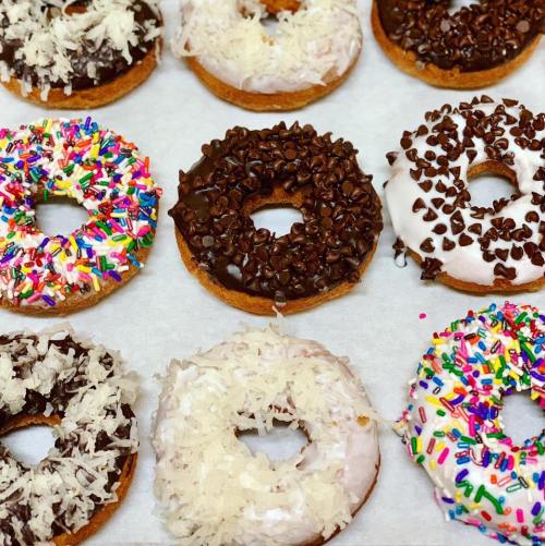 A variety of colorful donuts topped with chocolate, sprinkles, and coconut on a parchment paper background.