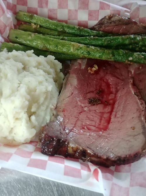 A plate featuring sliced roast beef, creamy mashed potatoes, and grilled asparagus on a checkered paper liner.