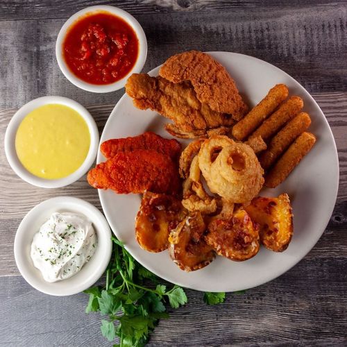 A plate of fried chicken, fish, onion rings, mozzarella sticks, and dipping sauces, garnished with fresh herbs.