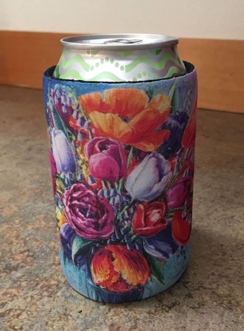 A colorful can cooler featuring a vibrant floral design, holding a soda can on a textured surface.