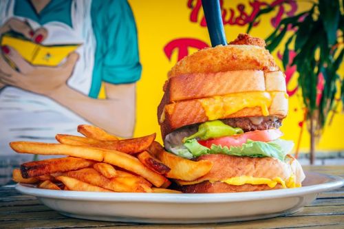 A towering burger with cheese, lettuce, and tomato, served with a side of golden fries against a colorful background.