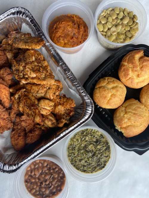 A spread of fried chicken, cornbread, greens, baked beans, pumpkin puree, and pumpkin seeds in various containers.