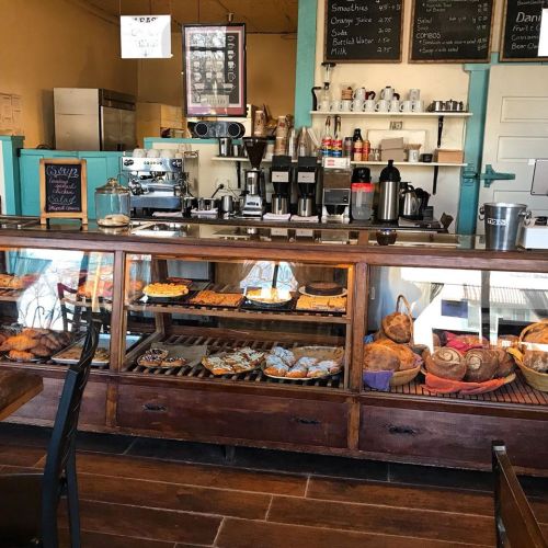 A cozy café interior featuring a display case of pastries and a coffee counter with various equipment and menus.