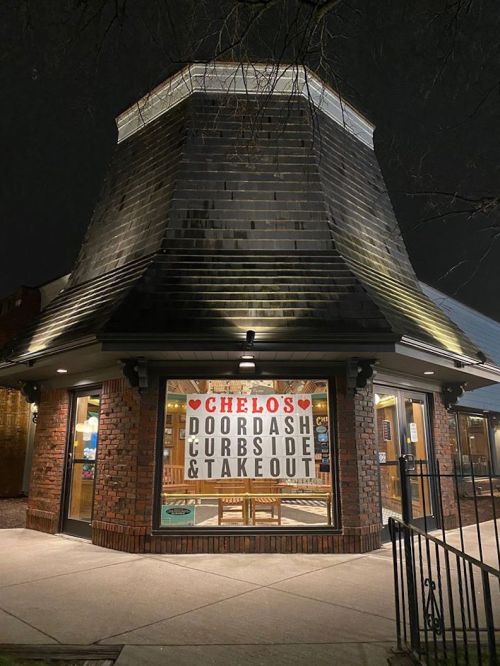 A brick building at night with a sign reading "Chelo's Doordash Curbside & Takeout" in the window.