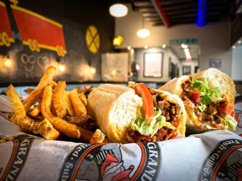 A close-up of a sandwich filled with meat, lettuce, and tomato, served with crispy fries on a paper-lined tray.