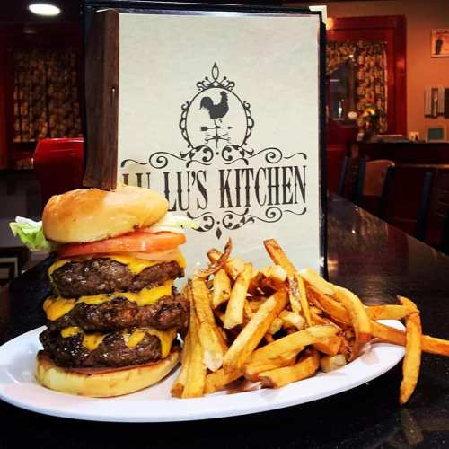 A towering cheeseburger with three patties, lettuce, and tomato, served with a side of golden fries.