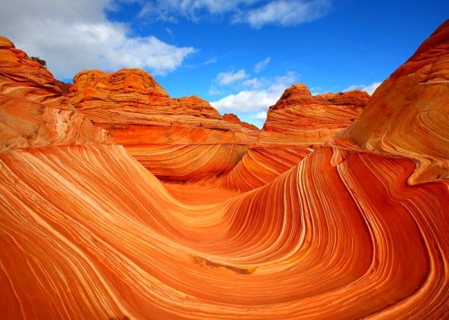 Vibrant orange and red rock formations with swirling patterns under a blue sky, showcasing natural erosion.