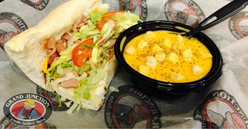 A sandwich filled with lettuce, tomatoes, and ham, served with a bowl of creamy cheese soup and croutons.