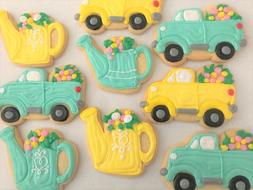 Colorful cookies shaped like vintage trucks and watering cans, decorated with flowers in yellow and turquoise icing.