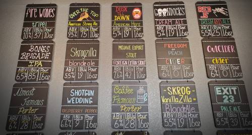 A chalkboard menu displaying various craft beers and ciders with names, ABV, and pour sizes.