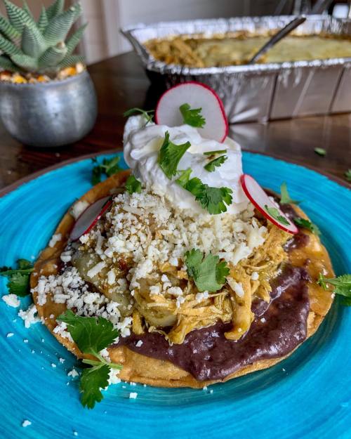 A colorful plate featuring a tostada topped with shredded chicken, black beans, sour cream, radishes, and cilantro.