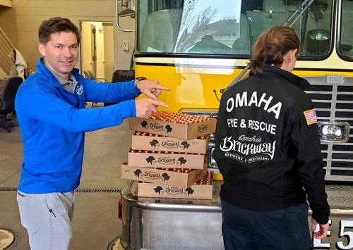 A man points at stacked boxes of food near a fire truck, while a firefighter in a jacket prepares to unload them.