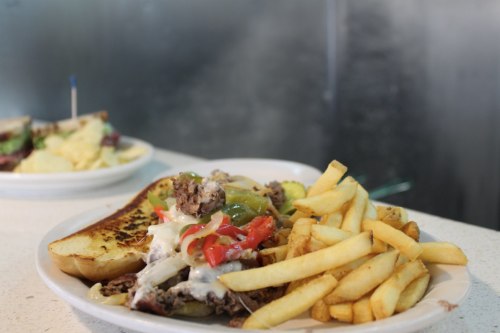 A plate of loaded cheesesteak with peppers and onions, served with crispy French fries on the side.