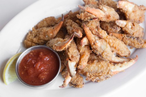A plate of crispy fried crab claws served with a side of tangy dipping sauce and a lemon wedge.
