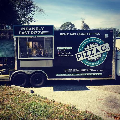 A black food truck with "Insanely Fast Pizza" and "Pizza Co." signage, parked in a sunny outdoor area.