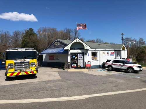 A fire truck and a police car parked outside a small building with an American flag, under a clear blue sky.