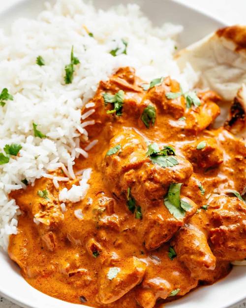 A bowl of creamy chicken curry with rice and naan, garnished with fresh cilantro.