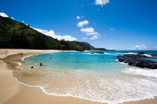 A serene beach with clear turquoise water, gentle waves, and people swimming under a bright blue sky.