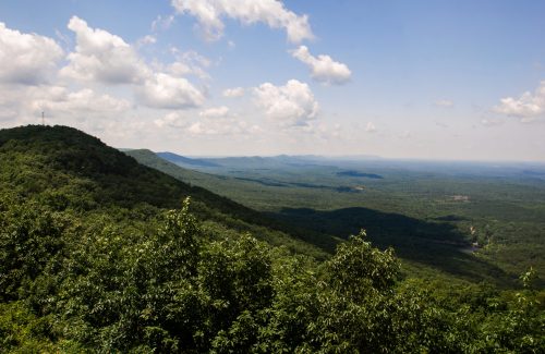 A panoramic view of lush green mountains under a blue sky with fluffy clouds.