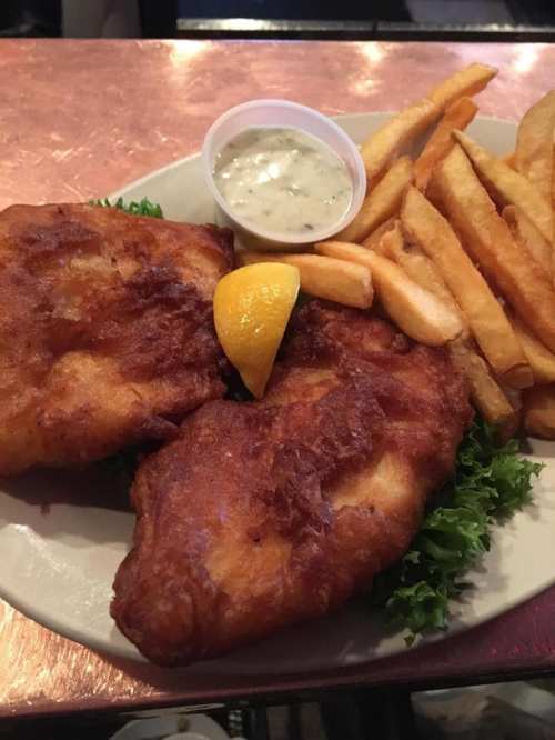 A plate of crispy fried fish fillets with a lemon wedge, served with fries and a side of tartar sauce on lettuce.