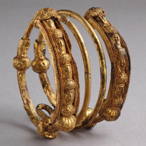 Three intricately designed gold bangles with decorative motifs and figures, showcasing ancient craftsmanship.