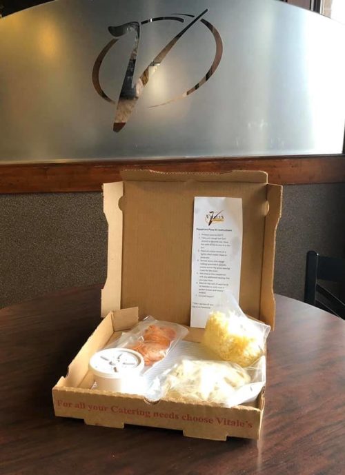 A takeout box with food items, including a container of sauce, cheese, and a menu, on a table in a restaurant.