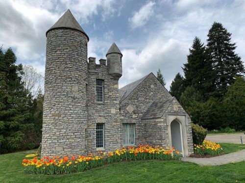 A stone castle with turrets surrounded by colorful tulips and lush greenery under a cloudy sky.