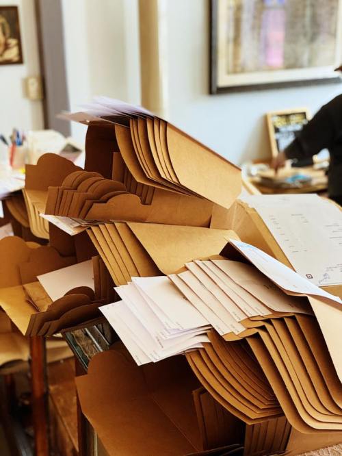 A cluttered table with stacked brown envelopes and scattered papers, creating a busy, organized chaos.