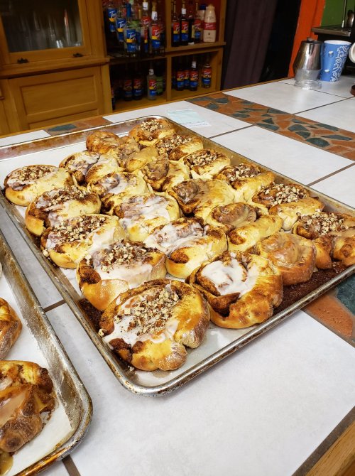 A tray of freshly baked cinnamon rolls topped with icing and nuts, arranged neatly on a table.