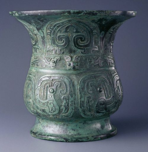 Ancient green bronze vessel with intricate carvings and a flared rim, showcasing detailed animal motifs.