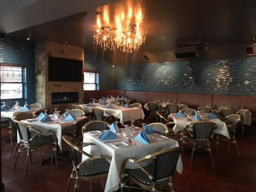 Elegant restaurant interior with blue decor, white tablecloths, and chandeliers, featuring neatly set tables.