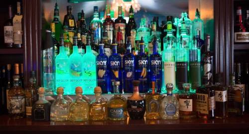 A well-stocked bar featuring various bottles of liquor, including vodka, tequila, and whiskey, with colorful lighting.