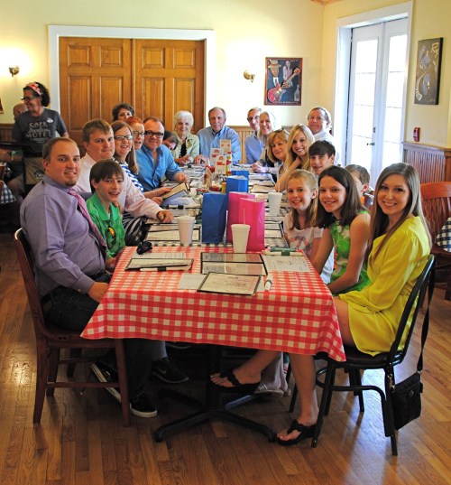 A large group of people gathered around a long table in a restaurant, smiling and enjoying their time together.