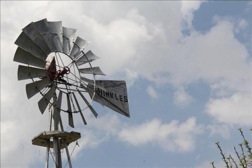 A vintage windmill with a weathered sign reading "SHINLES" against a backdrop of blue sky and fluffy clouds.