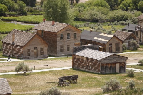 Aerial view of a historic ghost town with wooden buildings and a wagon in a grassy landscape.