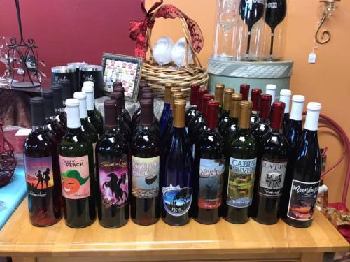 A display of various wine bottles with colorful labels arranged on a wooden table in a cozy setting.