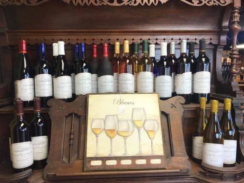 A wooden shelf displaying various bottles of wine and a painting of wine glasses.