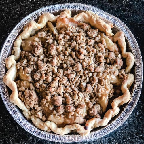 A freshly baked pie with a golden crust and a crumbly oat topping, placed in a silver pie dish.