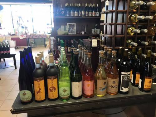 A display of various wine bottles in a store, featuring different colors and labels on a wooden shelf.