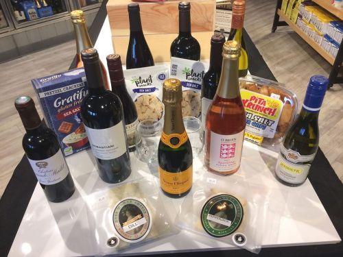 A variety of wines, snacks, and gourmet items displayed on a table, including crackers and spreads.