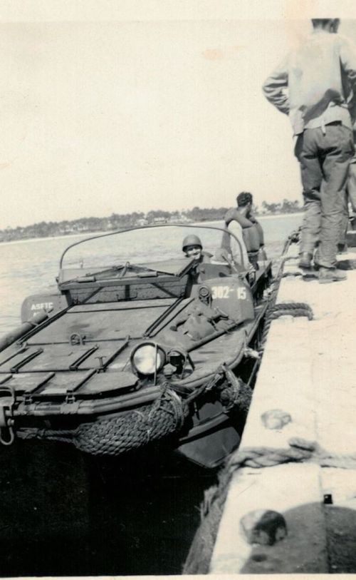 A military amphibious vehicle at a dock, with soldiers preparing for deployment on water.