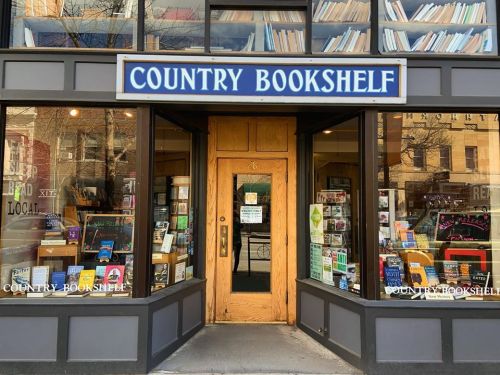 A cozy bookstore entrance with large windows displaying books and a sign reading "Country Bookshelf."