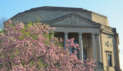 Severance Hall with blooming pink flowers in the foreground and a clear blue sky in the background.