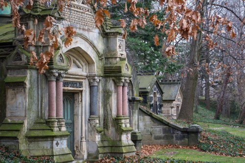 A serene cemetery scene featuring ornate mausoleums surrounded by autumn leaves and trees.
