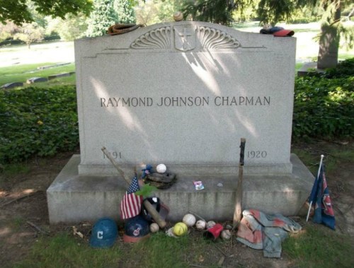 Gravestone of Raymond Johnson Chapman, 1891-1920, adorned with sports memorabilia and flags.