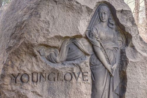A carved stone sculpture of a woman holding a staff, with the word "YOUNGLOVE" engraved below.