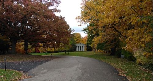 A winding path leads to a small white building surrounded by vibrant autumn trees in shades of orange and yellow.