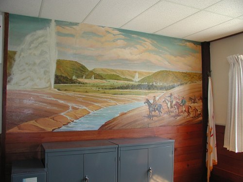 Mural depicting a scenic landscape with a waterfall, river, and horse riders in a room with wooden walls.