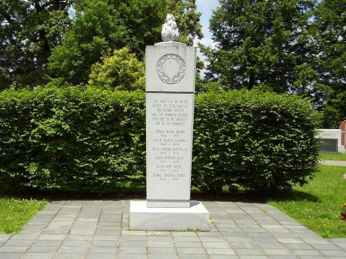 A stone monument with an inscription, surrounded by greenery and a pathway, commemorating individuals from a historical event.