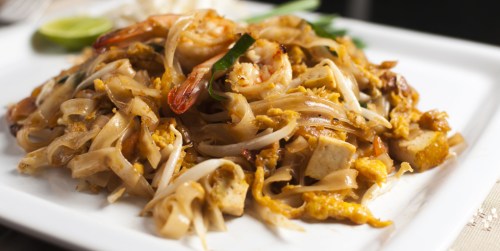 A plate of pad thai with shrimp, tofu, and bean sprouts, garnished with lime and green onions.